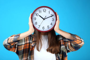 Genç Genç kız holding saat yüzünü mavi arka plan önünde