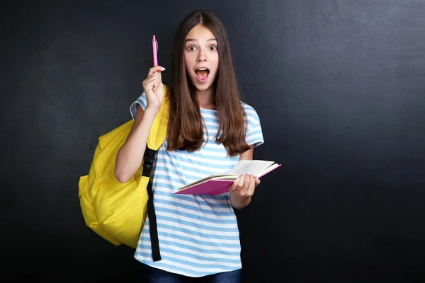 Junges Mädchen Mit Rucksack Und Buch Mit Stift Und Zeigefinger — Stockfoto