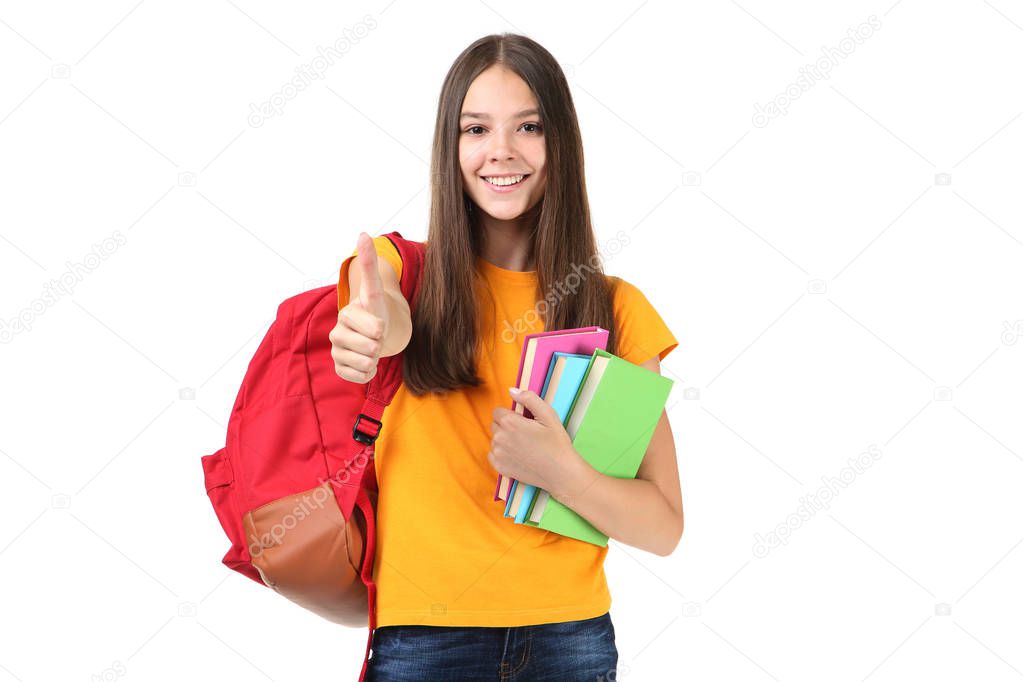 Young girl with backpack holding books and showing thumb up isolated on white background