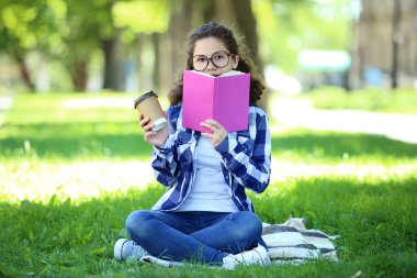 Kitap ve çim parkta oturup içki fincan genç kızla