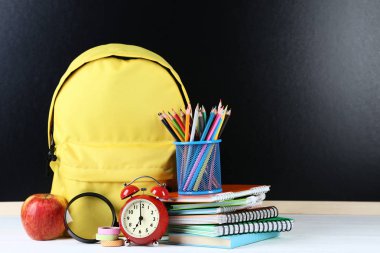Siyah zemin üzerine sarı sırt çantası ile okul malzemeleri
