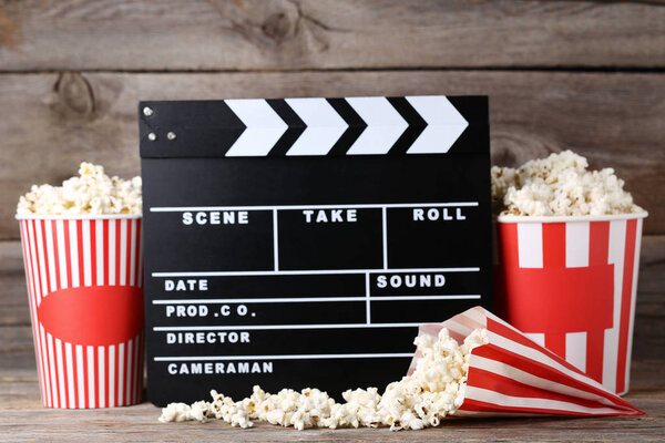 Clapper board with popcorn in striped buckets on wooden table