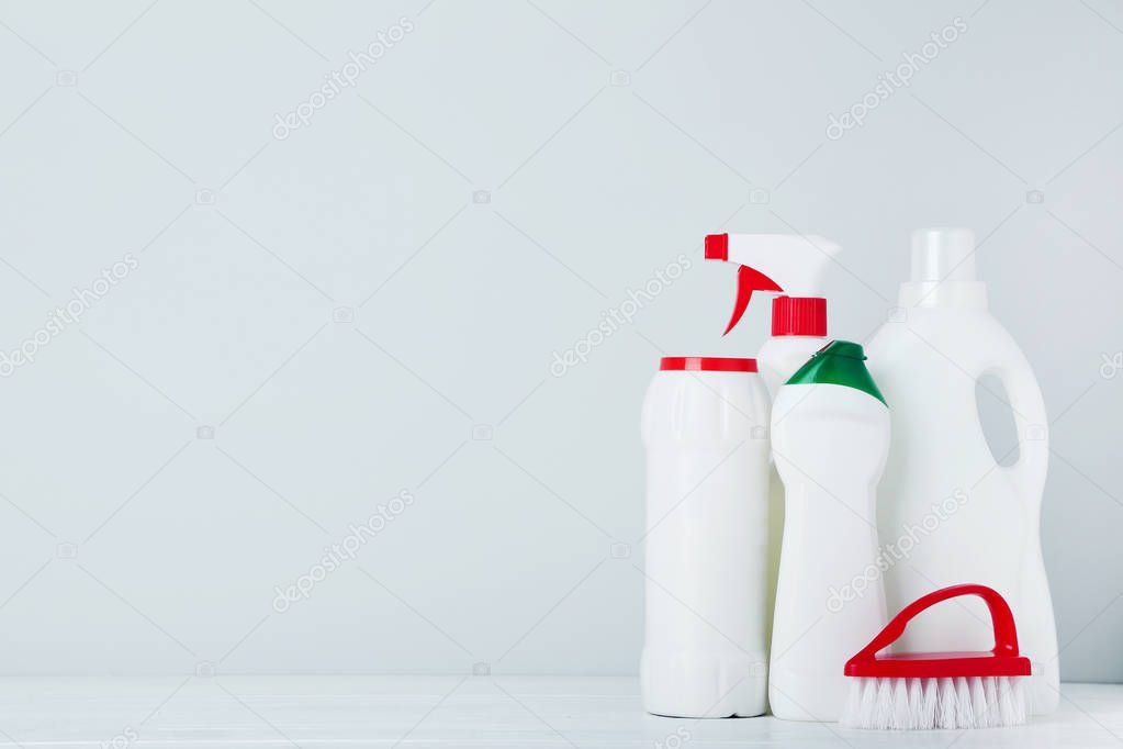 Bottles with detergent and brush on grey background