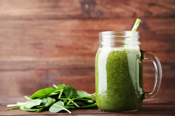 Spinach smoothie in glass jar on brown wooden table