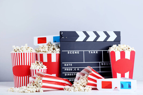 Clapper board with popcorn in striped buckets and glasses on grey background