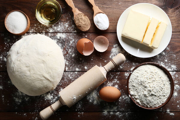 Raw dough with butter, eggs and rolling pin on wooden table