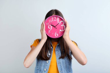 Gri arka plan üzerinde bir saat tutan genç kız