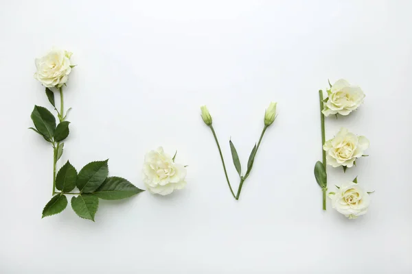 Inscription Love by flowers and green leafs on white background