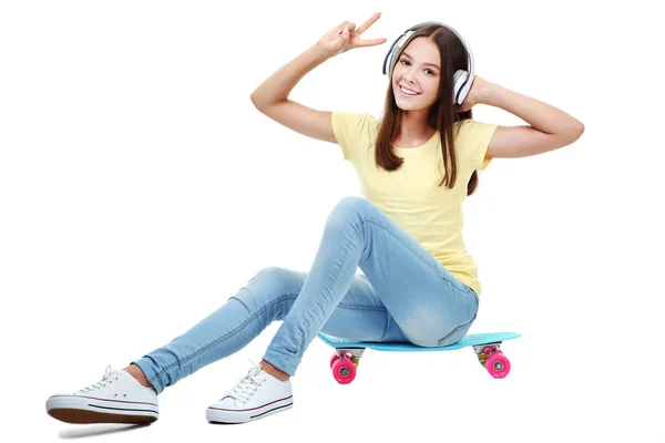 ヘッドフォンでスケート ボードに座っている若い女の子 — ストック写真