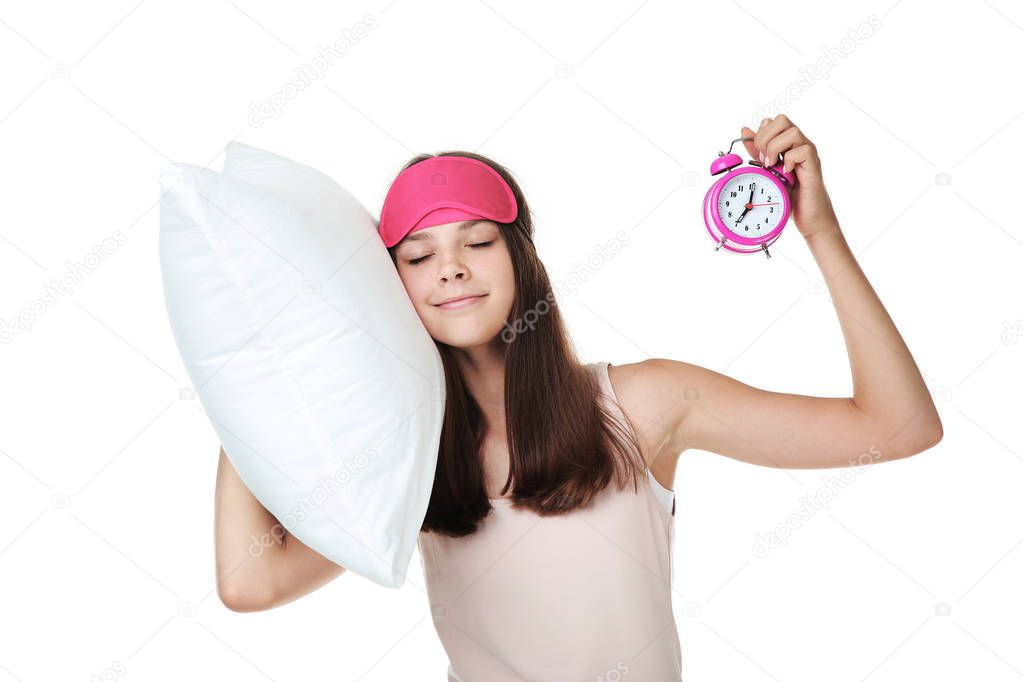 Young girl holding pillow and alarm clock on white background