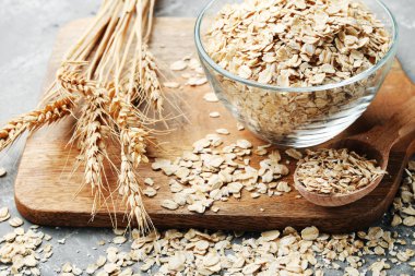 raw dry oatmeal in bowl on wooden chopping board clipart