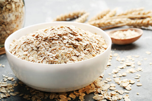 сухая сырая овсянка в белой миске на сером фоне

