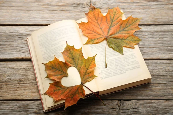 Dry maple leaves with cutout heart and open book on brown wooden table