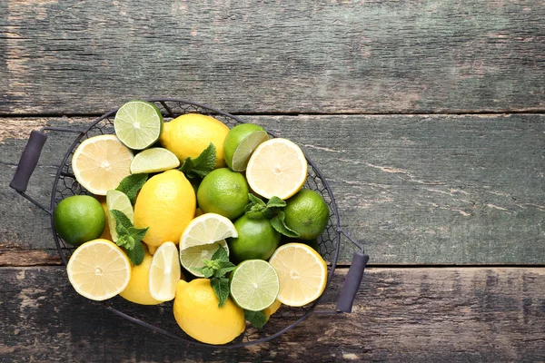 fresh whole and halved Lemons and limes with mint leaves in basket on grey wooden table