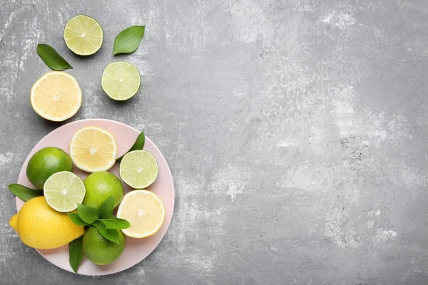 whole and halved Lemons and limes with green leaves on plate on grey background