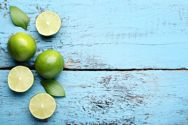 Ripe whole and halved limes with green leaves on blue wooden table