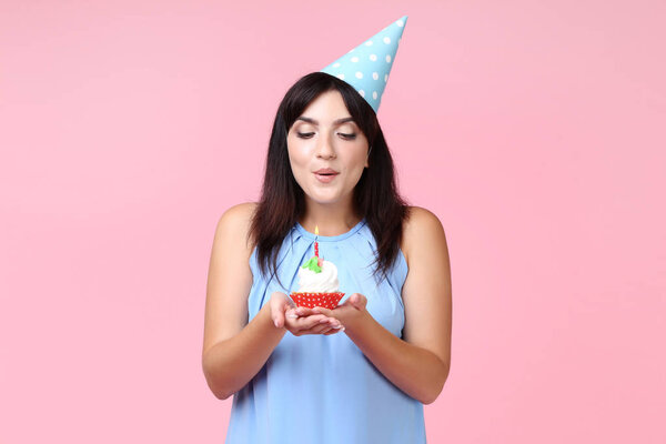 Young woman with birthday cupcake on pink background