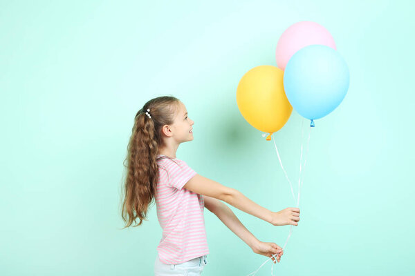 Cute young girl with colored balloons on mint background