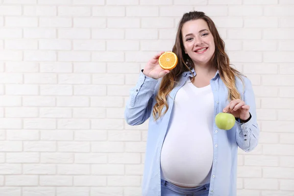 Schöne Schwangere Frau Mit Orangen Und Apfelfrüchten Auf Backsteinmauer Hintergrund — Stockfoto