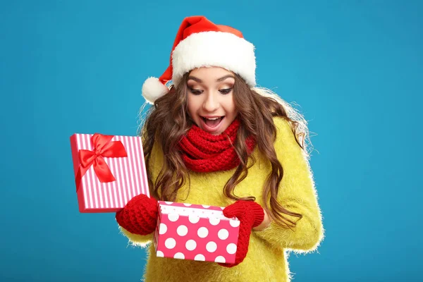美丽的年轻女孩在圣诞老人帽子与礼物箱子在蓝色背景 — 图库照片