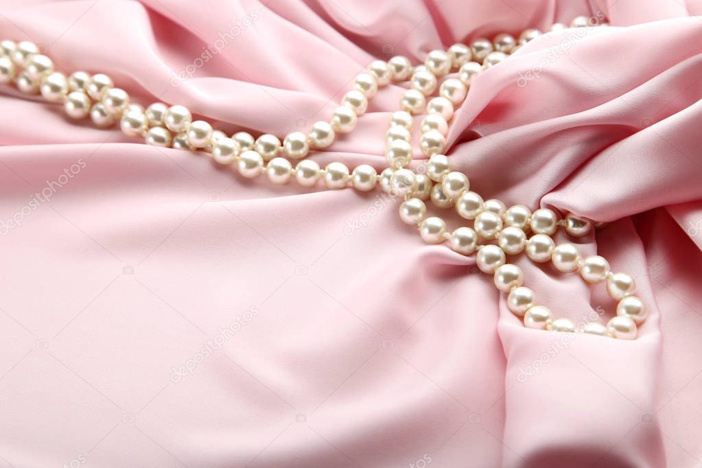 Pearl necklace on pink satin fabric