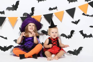 Cadılar Bayramı kostümleri beyaz arka plan üzerinde oturan küçük kızlar