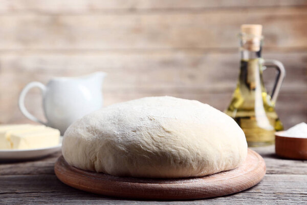 Сырое тесто с маслом на тарелке и бутылка масла на деревянном столе
