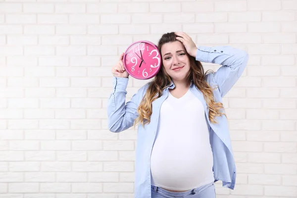 Hermosa Mujer Embarazada Sosteniendo Reloj Rosa Sobre Fondo Pared Ladrillo —  Fotos de Stock