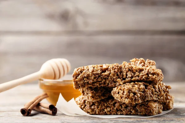 Tasty granola bars with honey in bowl and cinnamon on wooden background