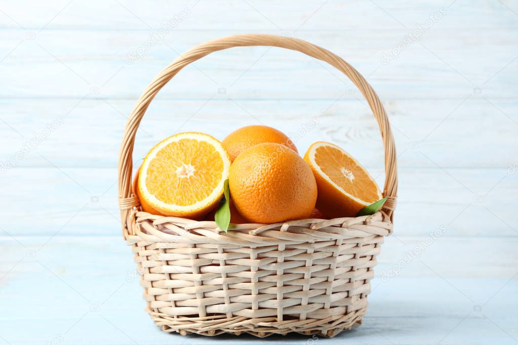 fresh whole and halved oranges with green leaves in basket on wooden table