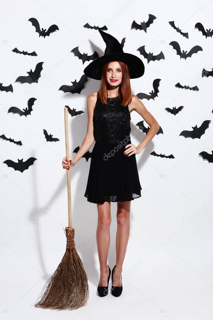 Beautiful redhaired woman with broom and paper bats on white background