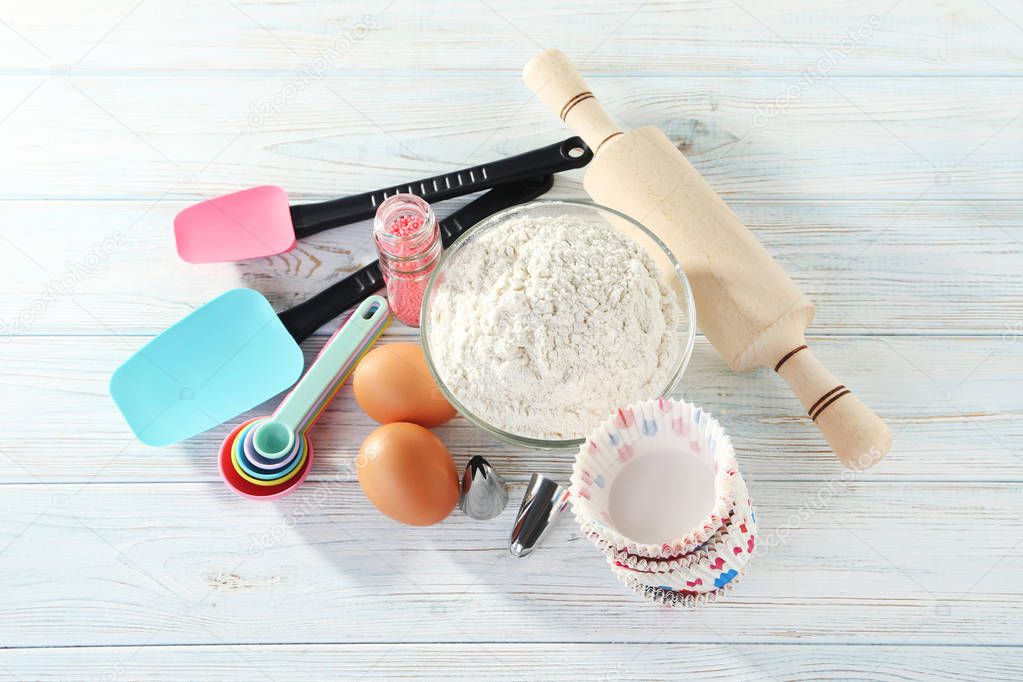 Empty cupcake cases with bowl of flour and eggs on white wooden table