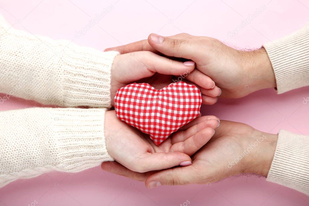 Female and male hand holding red checkered fabric heart on pink background