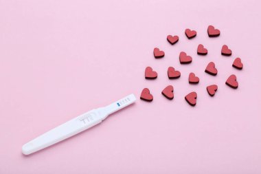 Pembe bir arka plan üzerinde kırmızı kalpler ile gebelik testi