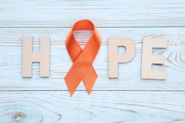 Orange ribbon with word Hope on wooden background clipart