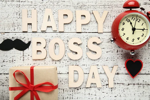 Inscription Happy Boss Day with alarm clock and gift box on grey wood