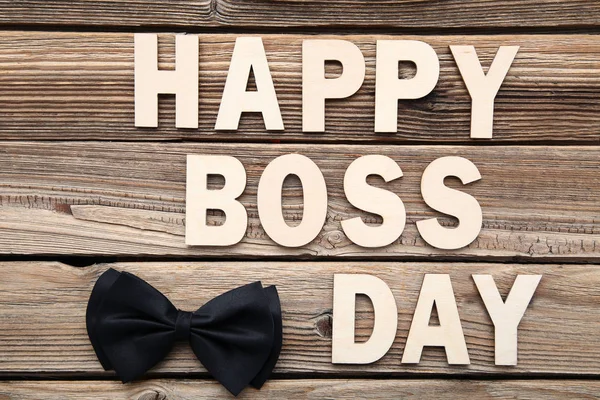 Inscription Happy Boss Day with bow tie on wooden table