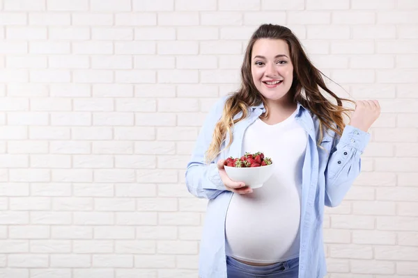 Hermosa Mujer Embarazada Con Fresas Tazón Sobre Fondo Pared Ladrillo —  Fotos de Stock