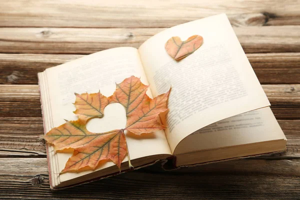 Dry maple leaf with heart and open book on brown wooden table