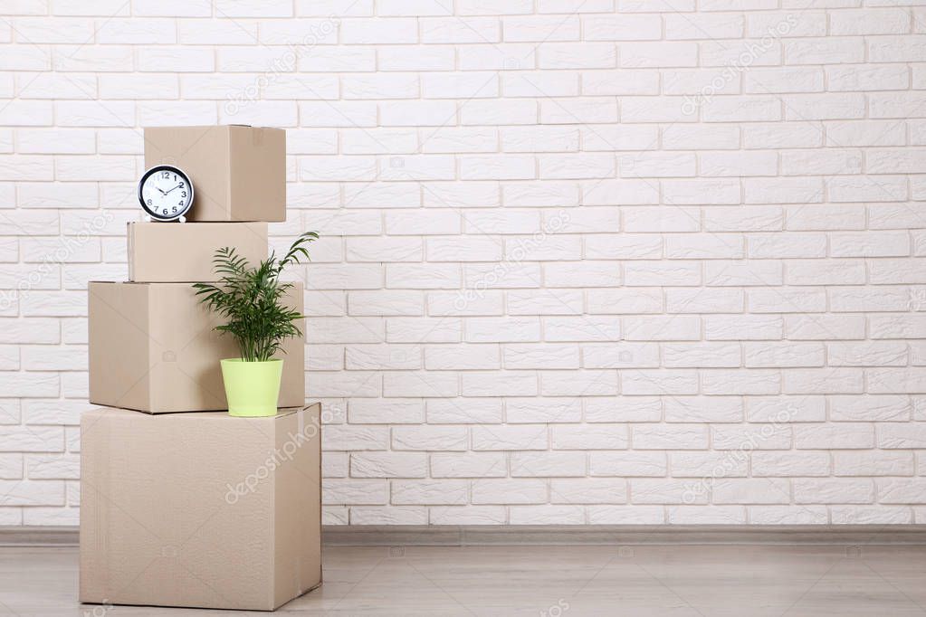 Cardboard boxes with clock and green plant on brick wall background