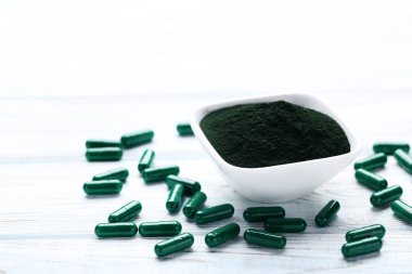 Spirulina tozu ve beyaz ahşap Ahşap üzerine kapsül