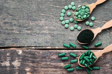 Spirulina tozu ve kaşık gri ahşap masa üzerinde hap