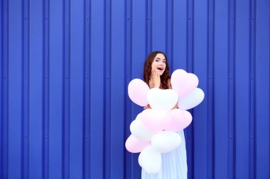Mavi arka plan üzerinde duran Kalp balonlar ile şirin kız