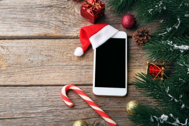 Ahşap masa kırmızı santa şapka ve köknar ağacı dalı ile Smartphone