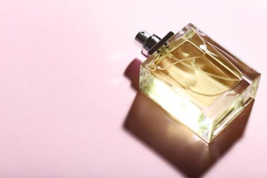 güneş ışığı altında pembe bir arka plan üzerinde parfüm şişesi