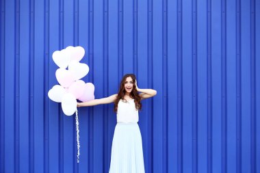 Mavi arka plan üzerinde duran Kalp balonlar ile şirin kız