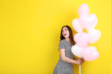 Sarı arka plan üzerinde duran Kalp balonlar ile çizgili elbiseli Genç kız