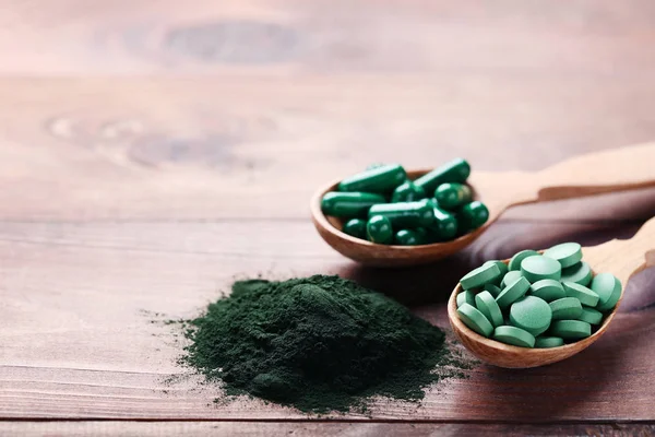 Spirulina powder and tablets in spoons on brown wooden table