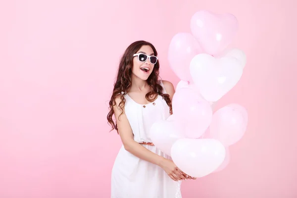 Young girl with heart-shaped balloons standing on pink background