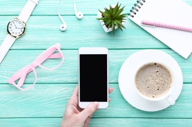 Kadın elinde fincan kahve, defter, ahşap masa üzerinde kol saati ile Smartphone